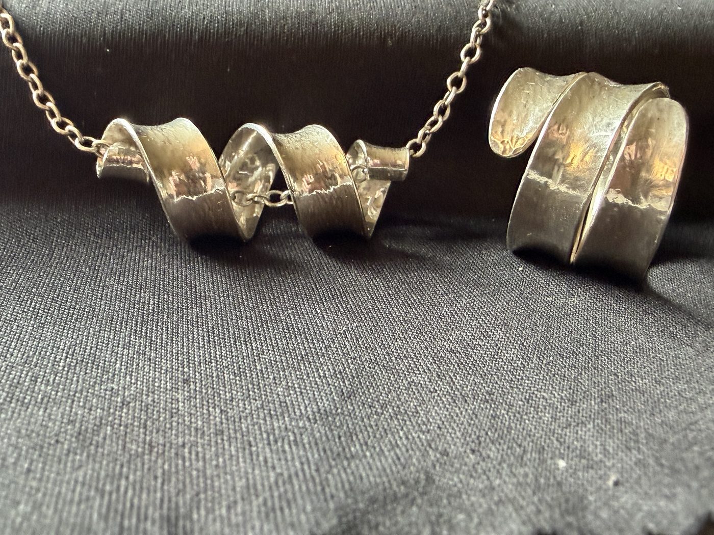 Spiral pendant and wrap ring side by side on black cloth